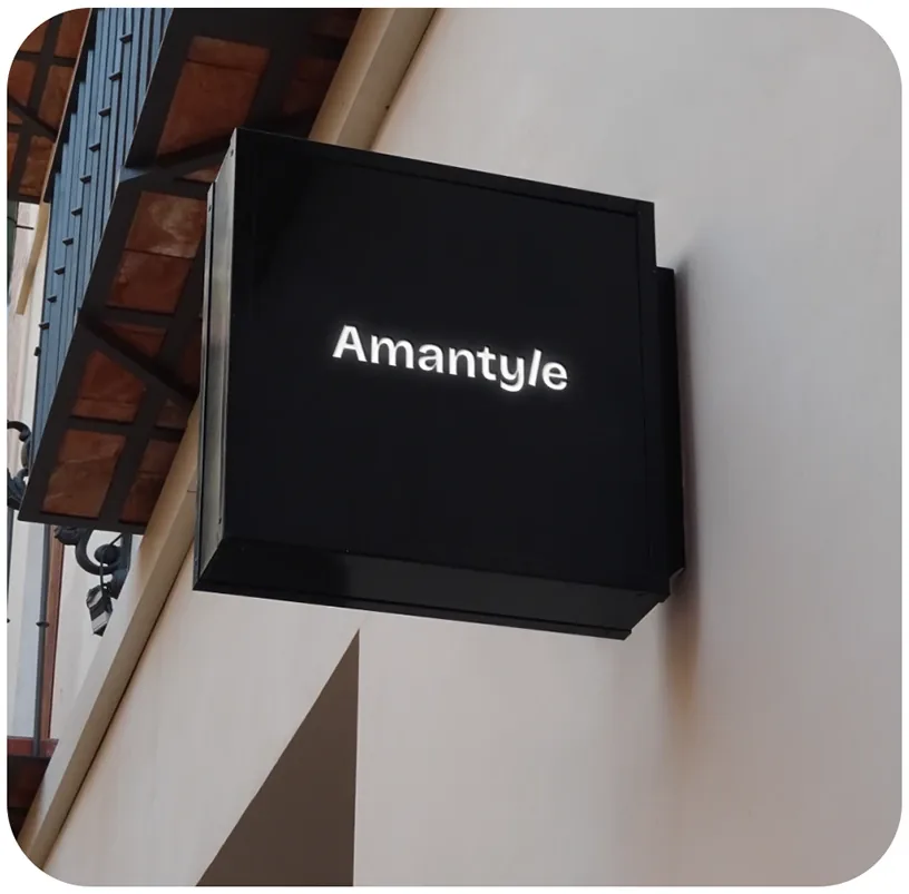A black box sign on a wall with the Amantyle wordmark lit in white.