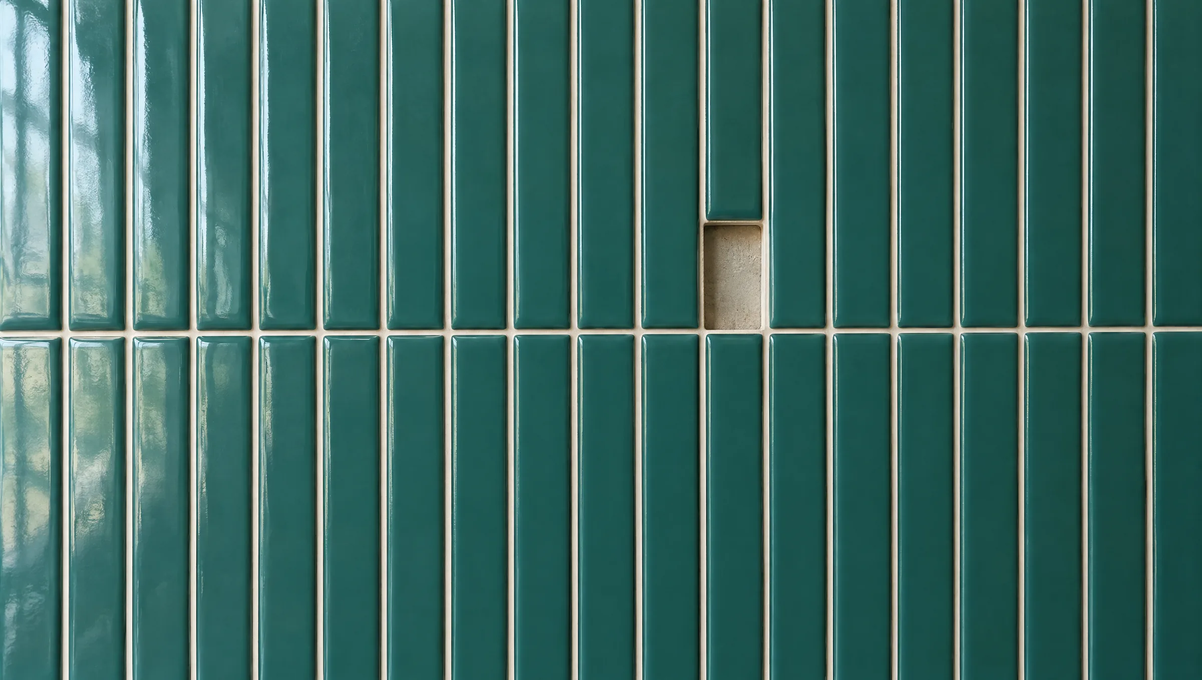 A wall of glossy teal finger tiles with a single tile missing, showing the bare wall behind