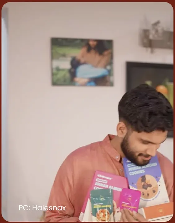 A smiling man in a coral shirt looking down at an armful of Halesnax packs, with the credit PC: Halesnax in the corner