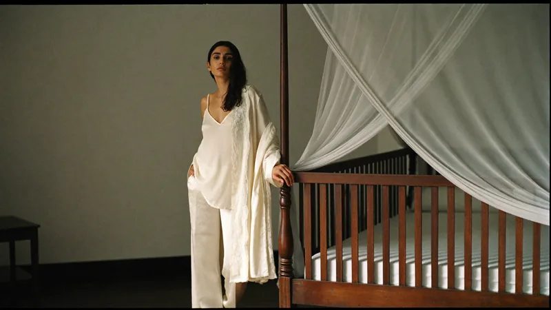 The set completer, in a robe over pyjamas beside a canopy bed, morning